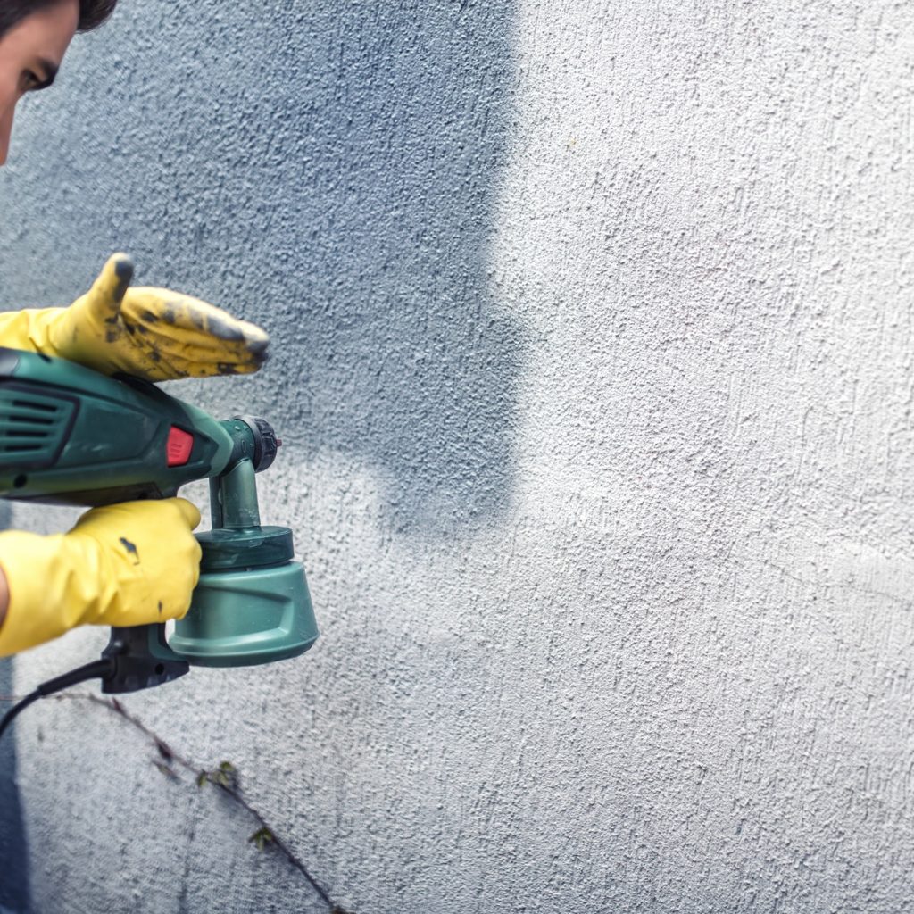 Man painting a grey wall, renovating exterior walls of new house